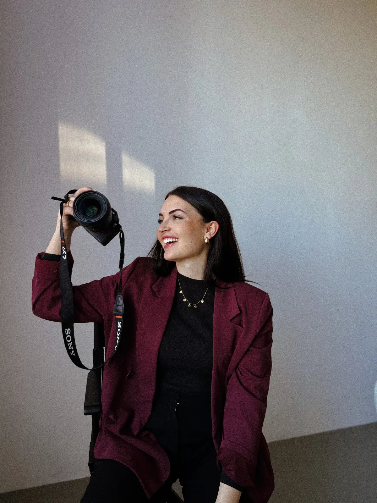 Anna-Lena Rumpler von ALR Media, lachend mit erhobener Kamera vor einer sonnenbeschienenen Wand