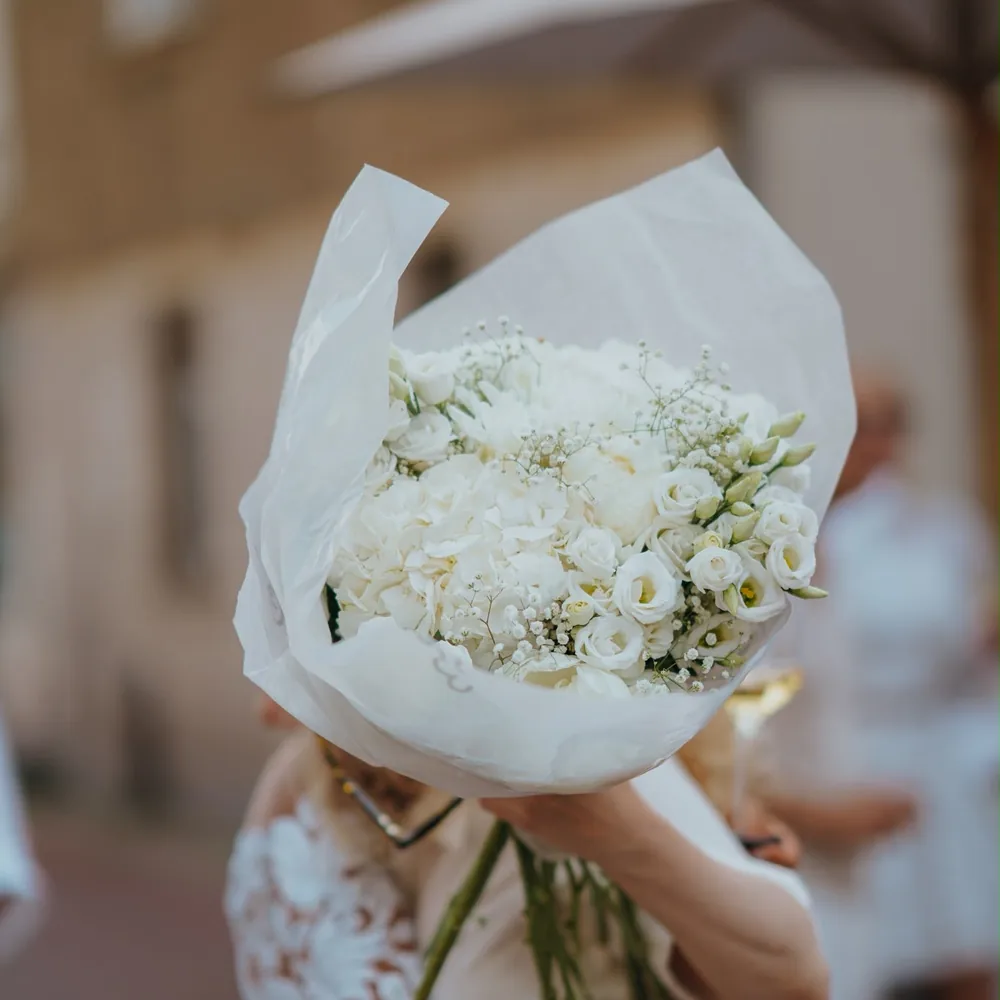 Weißer Brautstrauß aus Rosen und Schleierkraut, in Seidenpapier gehalten