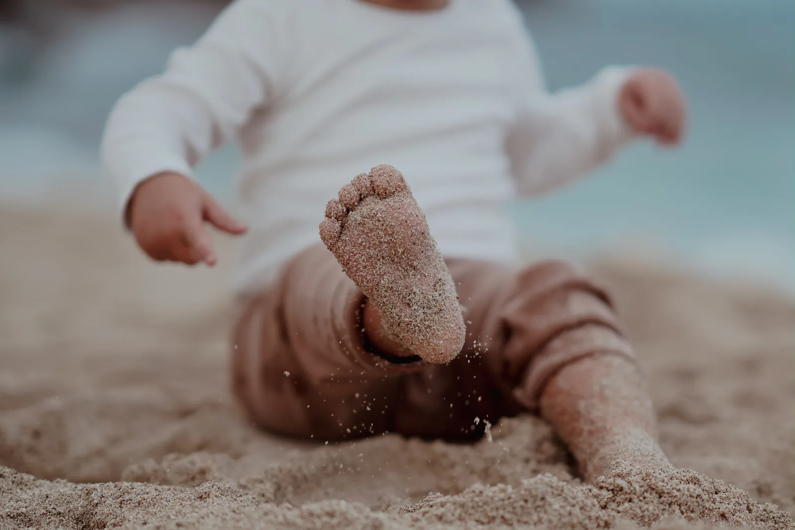 Kleinkind sitzt am Strand, die sandbedeckte Fußsohle ganz nah im Bild