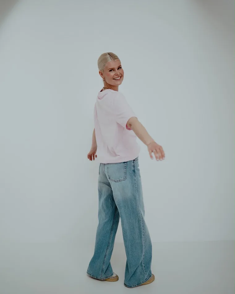Junge Frau in rosa Shirt und weiter Jeans dreht sich lachend über die Schulter um